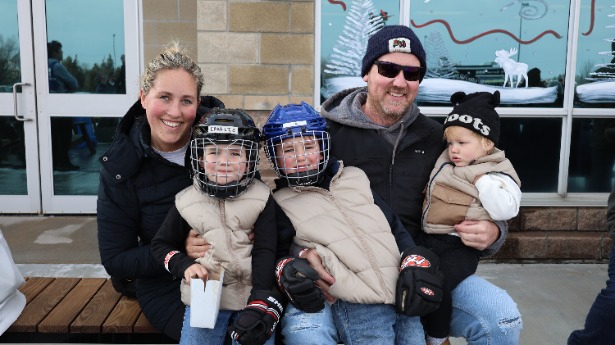 A family with children in skates and helmets on the bench beside the Courtice skating rink.
