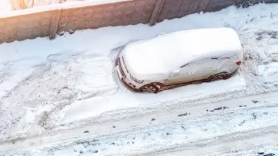 A car parked on the street snowed in by the snow plow.