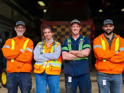 Four Clarington Staff in safety gear stand side by side in an industrial setting. Three wear orange jackets; one wears a blue uniform.
