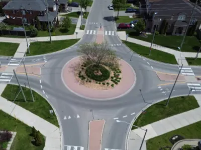 A roundabout in a residential area with houses nearby and sidewalks on either side.
