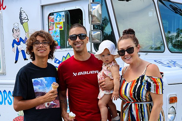 A family with children enjoying ice cream in front to the ice cream truck.