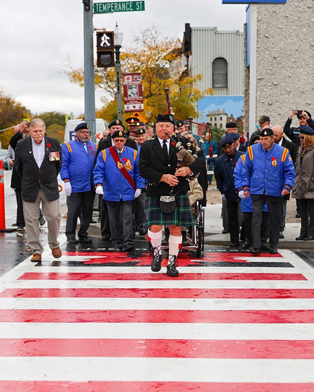 Piper Rick Paterson leads local veterans and Legion members across the crosswalk.