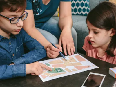 Two children and a parent review a home escape plan on their living room coffee table.