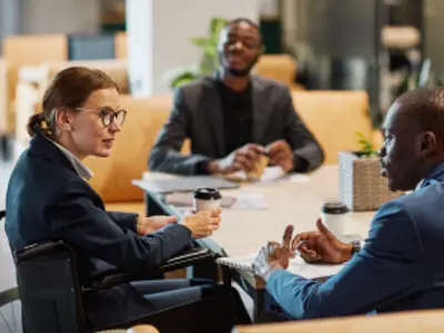 Side view portrait of successful businesswoman using wheelchair at meeting and talking to group of colleagues in modern office space.