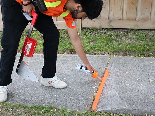 Clarington Summer Student spray painting a raised sidewalk.