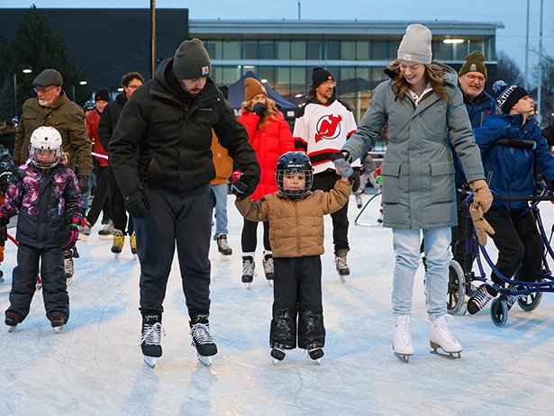 Parents holding their child's hand while skating around the rink with people skating in the background.