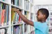 Young boy pulling a book off a library shelf.