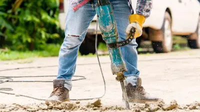 Worker uses a jack hammer on concrete making lots of noise.