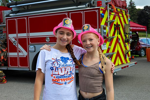 Two girls wearing fire hats pose in front to a fire truck.