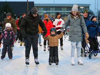 Parents holding their child's hand while skating around the rink with people skating in the background.